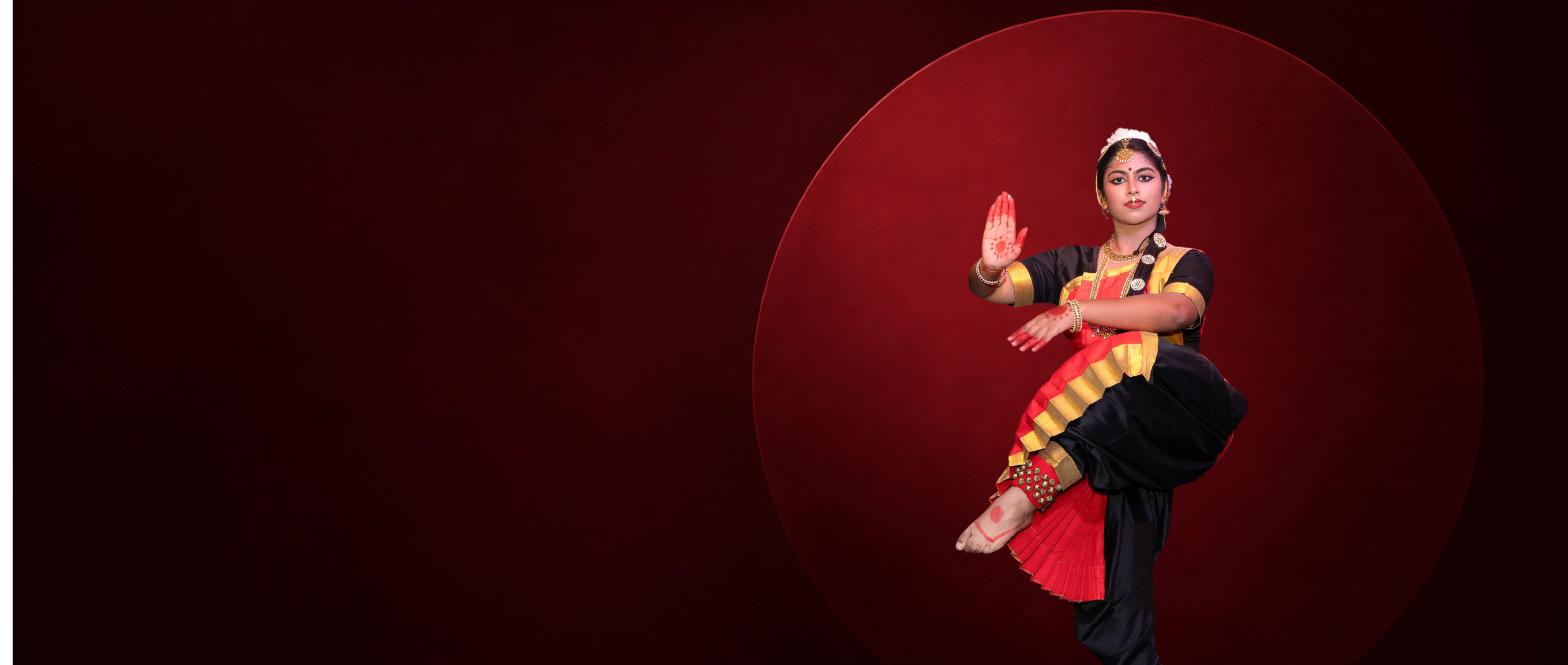 Bharatanatyam dancer in an emerald green and gold sari seated in araimandi before a deep maroon circle